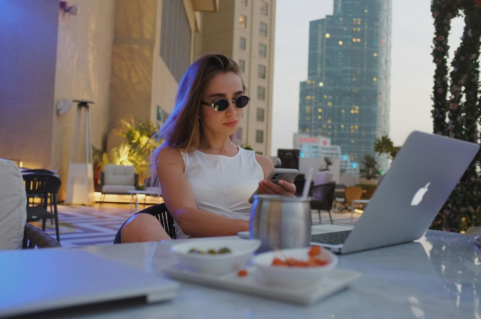 Woman using her phone and laptop at a rooftop café